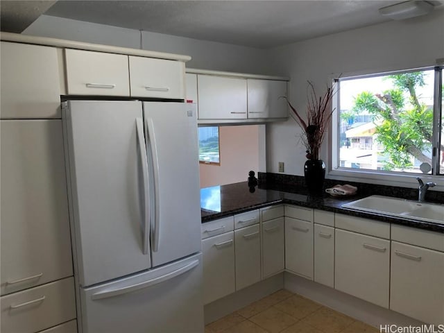 kitchen with light tile patterned floors, white fridge, white cabinetry, and sink