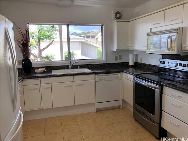 kitchen featuring dark stone counters, white appliances, sink, light tile patterned floors, and white cabinets