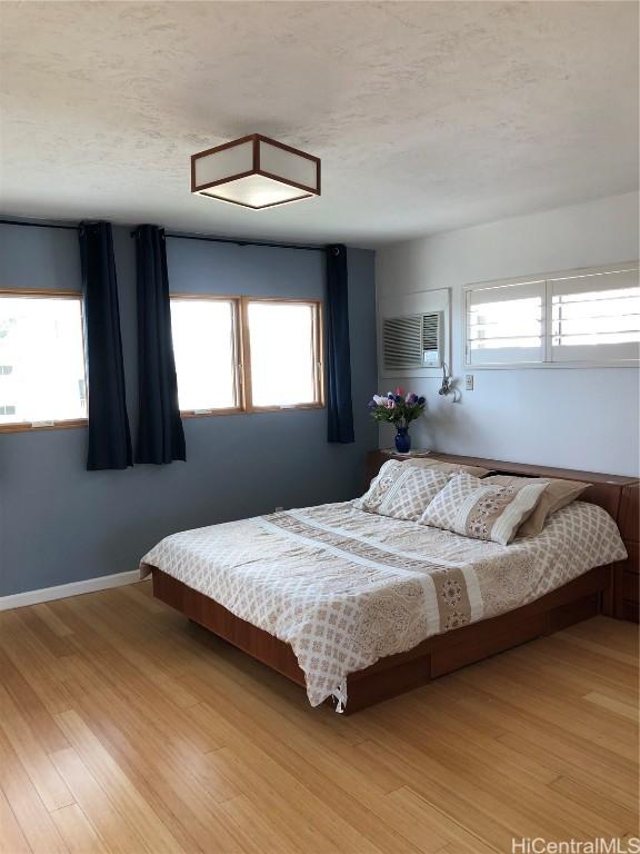 bedroom with a wall unit AC, multiple windows, light hardwood / wood-style floors, and a textured ceiling