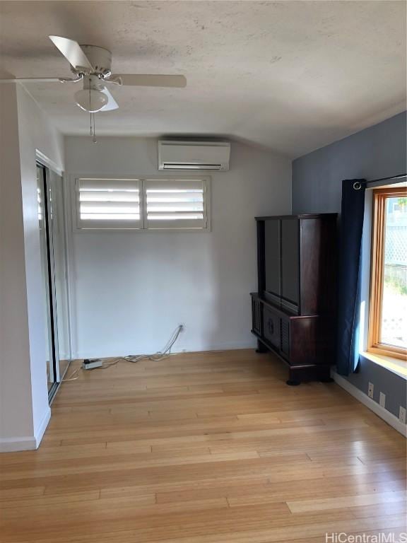 spare room with light hardwood / wood-style floors, a wall unit AC, ceiling fan, and lofted ceiling