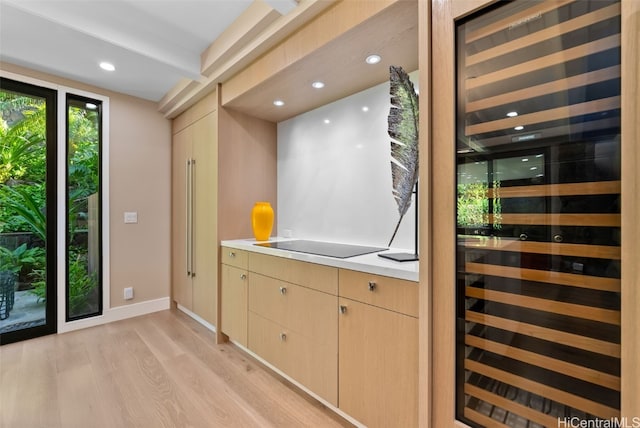 bar with light wood-type flooring, light brown cabinetry, beverage cooler, and black electric cooktop