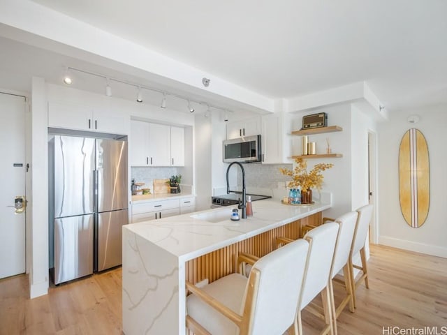 kitchen with light stone countertops, kitchen peninsula, tasteful backsplash, stainless steel appliances, and white cabinetry