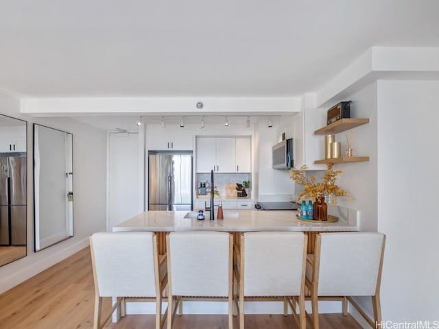 kitchen with kitchen peninsula, a kitchen breakfast bar, white cabinetry, and stainless steel refrigerator