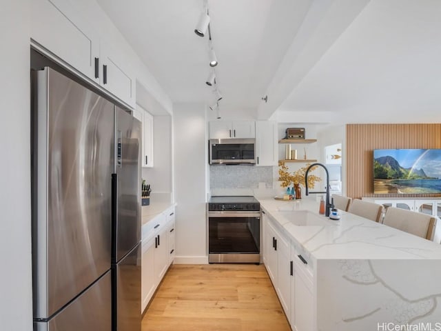 kitchen with light stone countertops, tasteful backsplash, stainless steel appliances, sink, and white cabinets