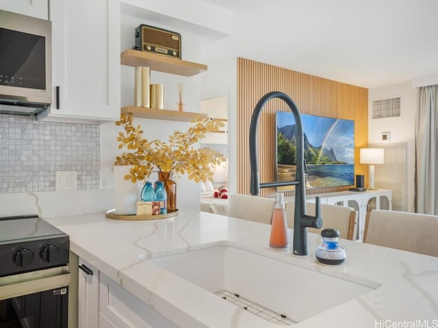 kitchen featuring tasteful backsplash, white cabinetry, sink, and light stone counters