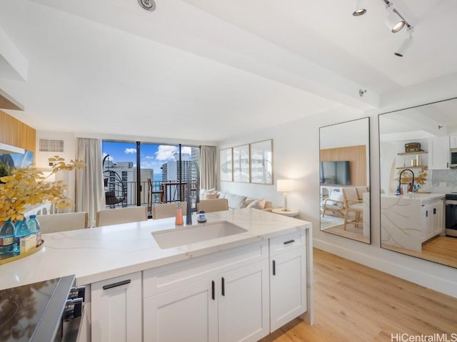 kitchen with light stone counters, white cabinetry, and sink