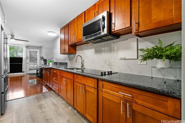 kitchen featuring sink, light wood-type flooring, dark stone counters, ceiling fan, and black electric cooktop