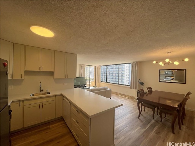 kitchen with sink, hanging light fixtures, hardwood / wood-style flooring, kitchen peninsula, and a chandelier