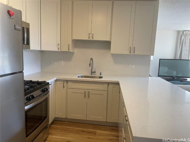 kitchen featuring light wood-type flooring, tasteful backsplash, light stone counters, stainless steel appliances, and sink