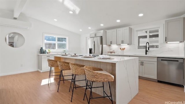 kitchen featuring appliances with stainless steel finishes, a wall mounted AC, a breakfast bar, a kitchen island, and sink