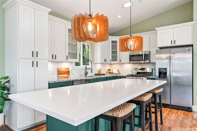 kitchen with a center island, white cabinets, vaulted ceiling, decorative light fixtures, and stainless steel appliances