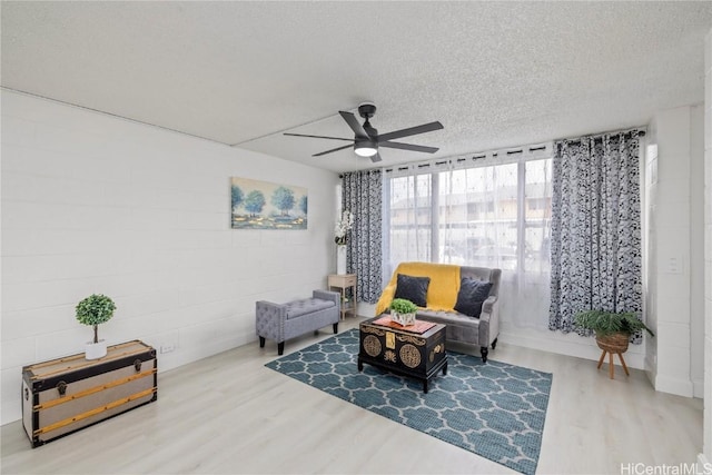 living area with ceiling fan, wood-type flooring, and a textured ceiling