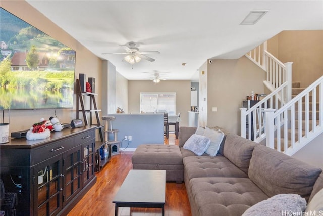 living room with ceiling fan, visible vents, wood finished floors, and stairs