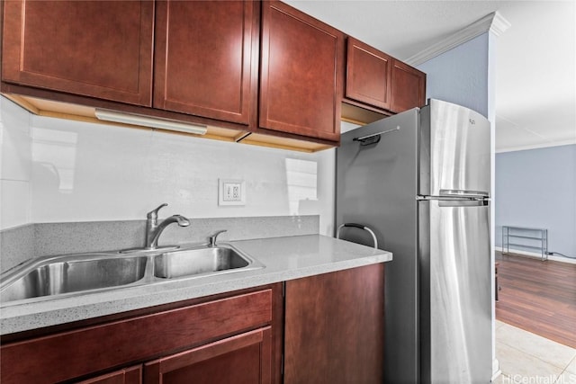 kitchen with light tile patterned floors, stainless steel refrigerator, ornamental molding, and sink