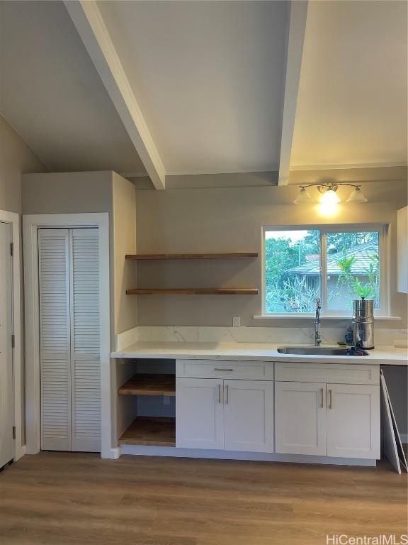 kitchen featuring white cabinets, beam ceiling, light hardwood / wood-style flooring, and sink