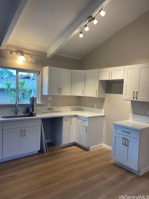 kitchen featuring white cabinets, wood-type flooring, vaulted ceiling with beams, and sink