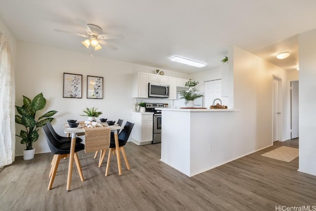 kitchen with white cabinets, ceiling fan, appliances with stainless steel finishes, light hardwood / wood-style floors, and kitchen peninsula