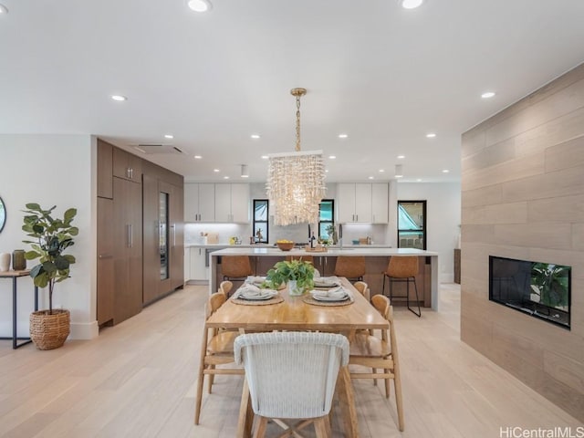 dining area featuring light wood-type flooring, a fireplace, a wealth of natural light, and a chandelier