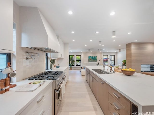 kitchen featuring white cabinetry, stainless steel range, sink, premium range hood, and light hardwood / wood-style floors