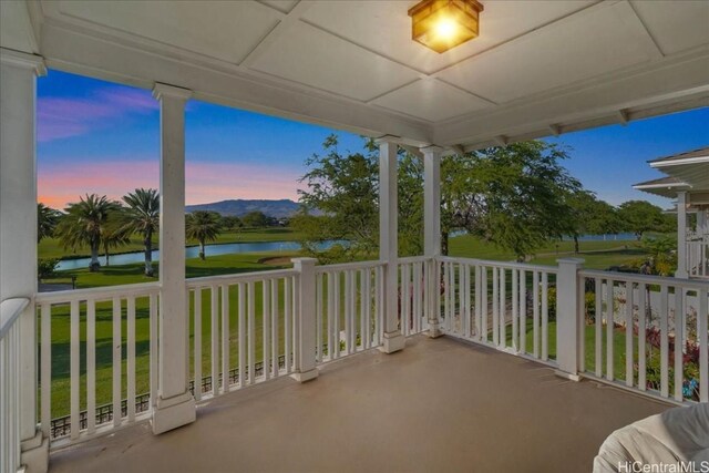 balcony at dusk with covered porch and a water view