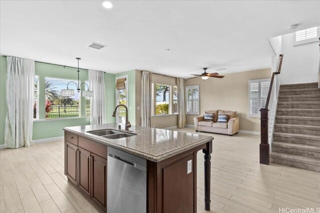 kitchen featuring dishwasher, sink, an island with sink, decorative light fixtures, and light stone counters