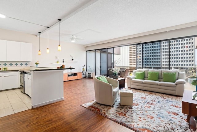 living room with ceiling fan, a textured ceiling, and light hardwood / wood-style flooring