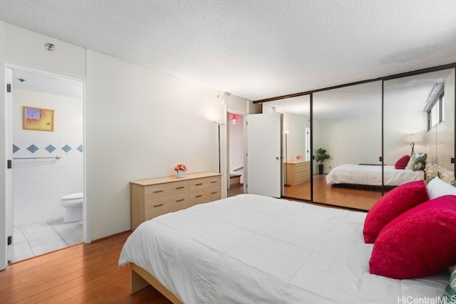 bedroom featuring ensuite bathroom, a textured ceiling, tile walls, light hardwood / wood-style floors, and a closet