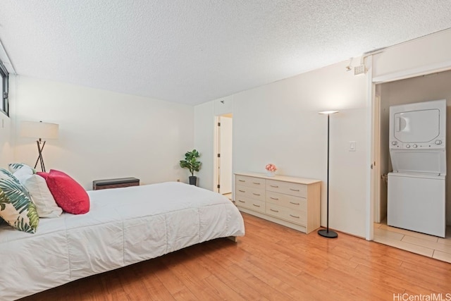 bedroom featuring light hardwood / wood-style floors, stacked washing maching and dryer, and a textured ceiling