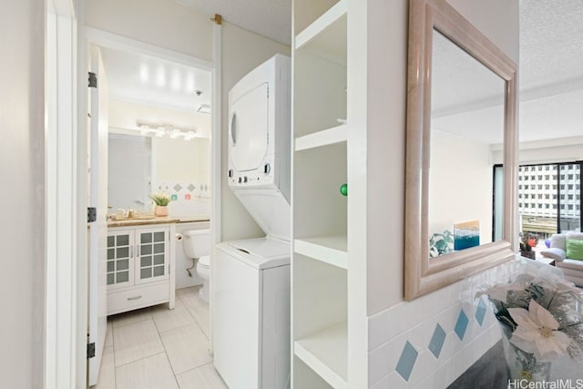 laundry area featuring stacked washing maching and dryer, a textured ceiling, sink, tile walls, and light tile patterned flooring