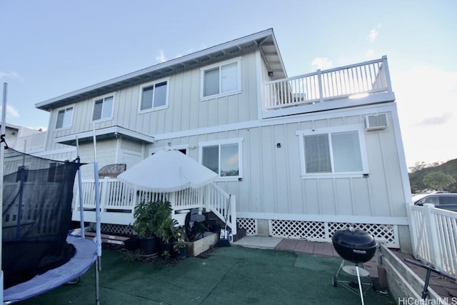 rear view of house featuring a trampoline, a balcony, an AC wall unit, and a lawn