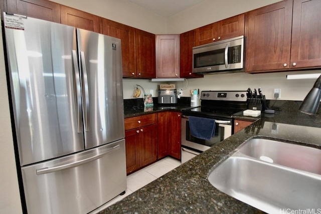 kitchen featuring sink, light tile patterned flooring, dark stone countertops, and stainless steel appliances