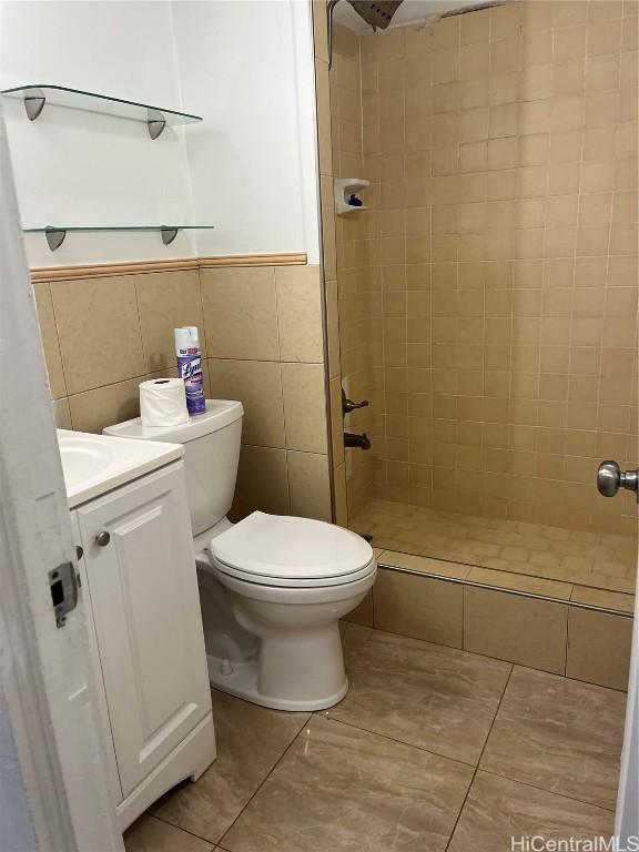 bathroom featuring tile patterned flooring, tiled shower, toilet, vanity, and tile walls