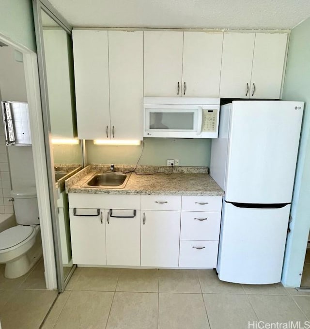 kitchen with white cabinets, light tile patterned floors, white appliances, and sink