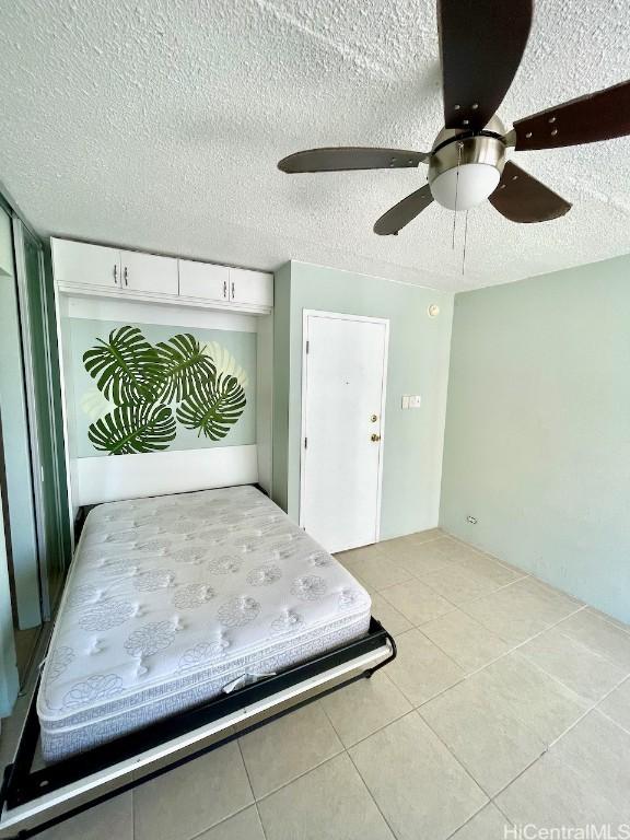 unfurnished bedroom featuring light tile patterned floors, a textured ceiling, and ceiling fan