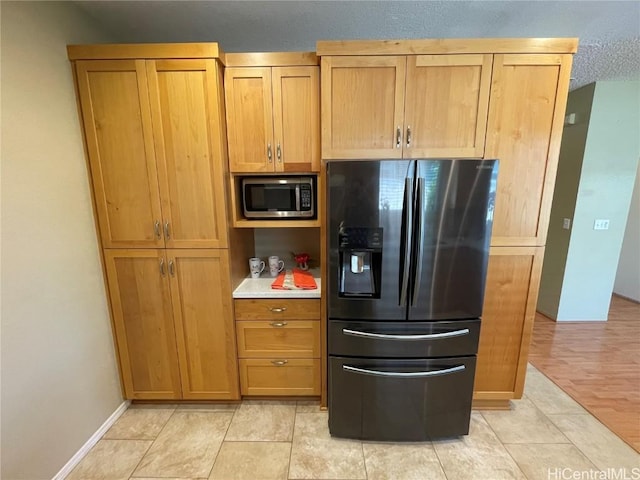 kitchen featuring black fridge with ice dispenser, light hardwood / wood-style floors, and a textured ceiling