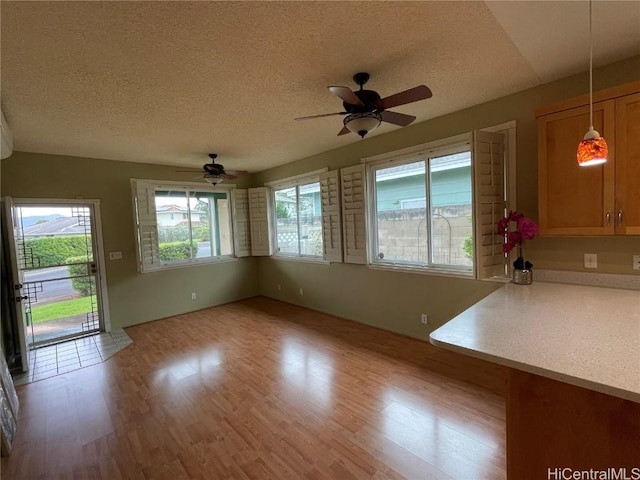 unfurnished dining area with ceiling fan, a textured ceiling, and light wood-type flooring