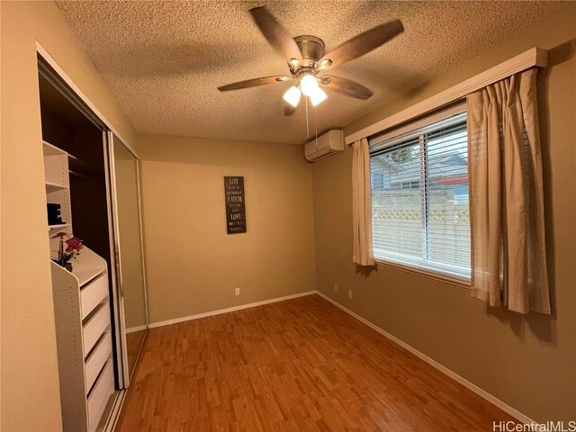 unfurnished bedroom featuring hardwood / wood-style flooring, ceiling fan, a textured ceiling, a wall mounted AC, and a closet