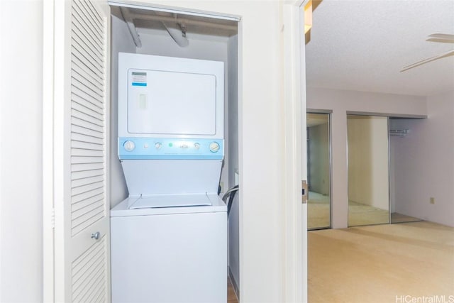 washroom featuring ceiling fan, a textured ceiling, and stacked washer and clothes dryer