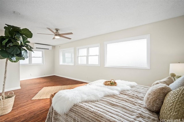 bedroom featuring hardwood / wood-style floors, ceiling fan, a textured ceiling, and a wall unit AC