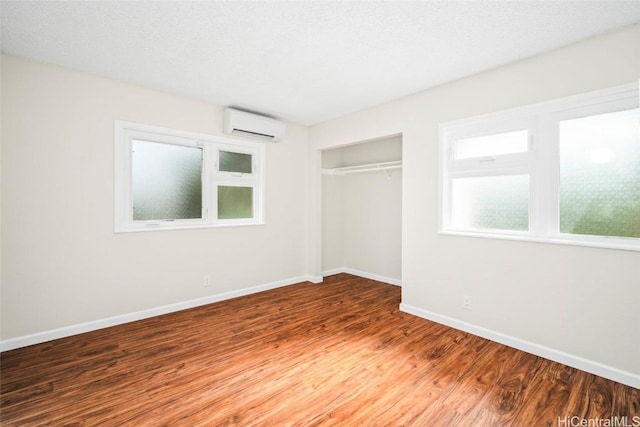 unfurnished bedroom featuring a textured ceiling, hardwood / wood-style flooring, an AC wall unit, and a closet