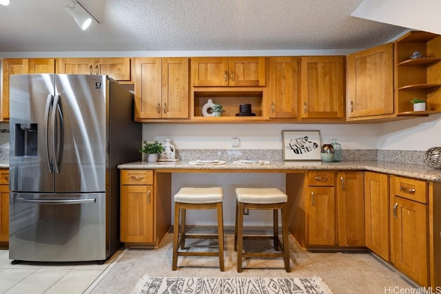 kitchen featuring track lighting, stainless steel fridge, light stone countertops, a textured ceiling, and light tile patterned floors