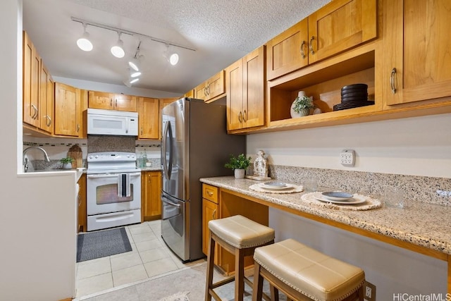 kitchen with a kitchen bar, light stone countertops, a textured ceiling, white appliances, and light tile patterned flooring