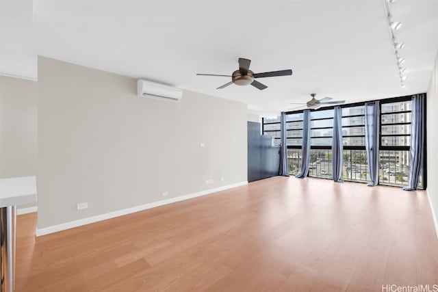 unfurnished living room featuring rail lighting, expansive windows, a wall unit AC, ceiling fan, and light hardwood / wood-style flooring