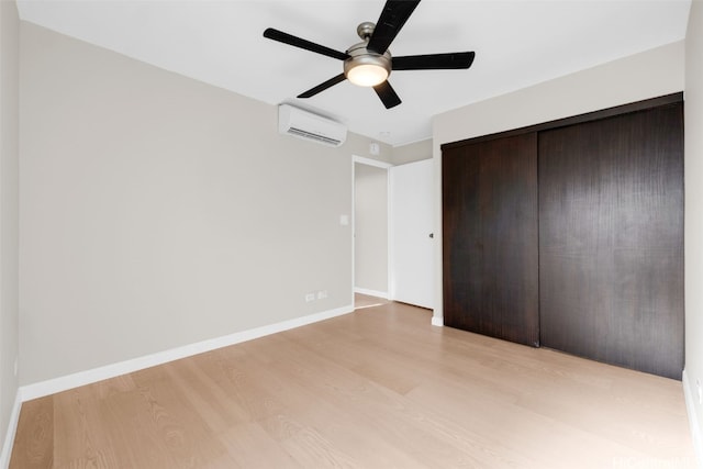 unfurnished bedroom with a wall unit AC, ceiling fan, a closet, and light wood-type flooring