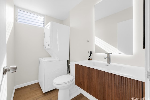 bathroom with stacked washer and dryer, vanity, wood-type flooring, and toilet