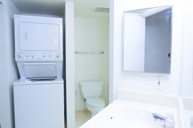 bathroom with a sink, toilet, stacked washer / dryer, and visible vents