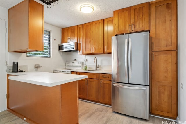 kitchen with kitchen peninsula, a textured ceiling, stainless steel appliances, sink, and light hardwood / wood-style floors