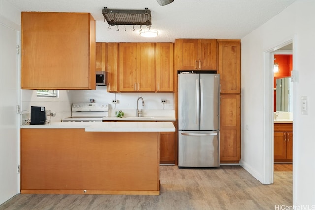 kitchen with sink, stainless steel appliances, kitchen peninsula, light hardwood / wood-style floors, and a textured ceiling