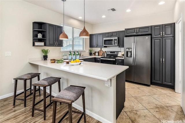 kitchen with kitchen peninsula, a kitchen breakfast bar, stainless steel appliances, pendant lighting, and light tile patterned flooring