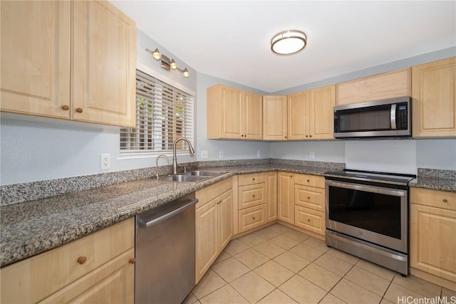 kitchen featuring light brown cabinetry, sink, light tile patterned floors, dark stone countertops, and stainless steel appliances